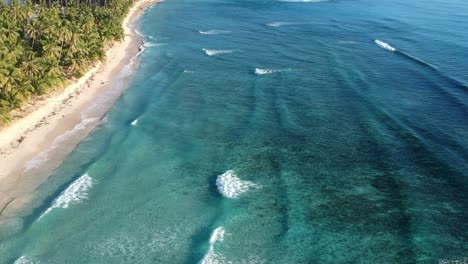 Aerial-shot-of-beautiful-waves-by-the-tropical-white-sand-beach-ideal-for-surfing
