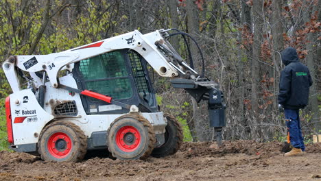 Hydraulic-auger-mounted-on-skid-steer-loader-is-removed-from-posthole-and-auger-spins-to-remove-wet-dirt-from-auger