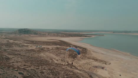 Aerial-Drone-Shot-Of-A-Paraglider-Landing-Beside-Salt-Lake-In-Karachi
