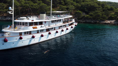 Tourist-Swimming-At-The-Ocean-Beside-The-Passenger-Boat-At-Paklinski-Island,-Hvar,-Croatia