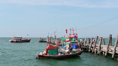 Barcos-De-Pesca-Atracados-Y-Moviéndose-Con-Las-Olas-Mientras-La-Gente-Tiende-A-Abastecerse-En-El-Muelle-De-Pesca-De-Pattaya,-Chonburi,-Tailandia