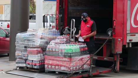 Man-reviewing-invoice-standing-near-pallets-of-Coke-products-and-a-delivery-truck-with-Coca-Cola-logo