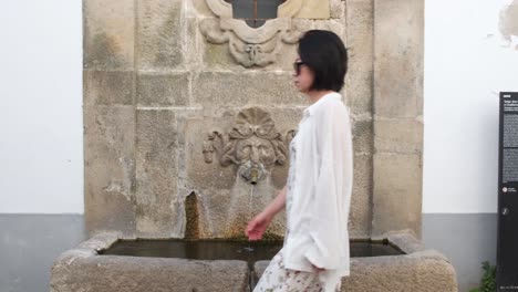 Woman-walking-in-Monsanto-village-with-old-fountain-in-background,-Portugal