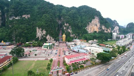 Weitwinkelantenne-Umkreist-Den-Eingang-Zu-Den-Berühmten-Batu-Höhlen-In-Kuala-Lumpur,-Malaysia,-An-Einem-Bewölkten-Nachmittag-Mit-Autobahnverkehr-In-Der-Nähe-Und-Großen-Kalksteinbergen-In-Der-Ferne