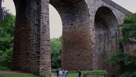Large-arched-bridge-shot-frpm-low-down-with-moving-trees-and-walkers-passing-by