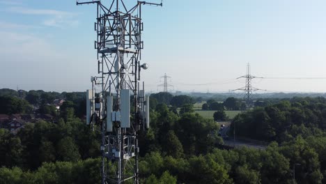 5G-broadcasting-tower-antenna-in-British-countryside-with-vehicles-travelling-on-highway-background-aerial-zoom-out-view