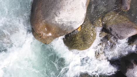 Aerial-shot-of-water-stream-flowing-near-the-rocks-and-mountain-in-the-background