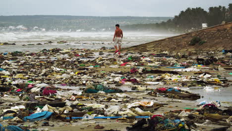 Oben-ohne-Mann,-Der-An-Einem-Düsteren-Tag-Am-Schmutzigen,-Verschmutzten-Strand-Voller-Müll-Spaziert