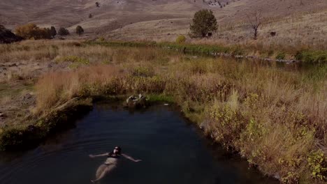 flyover-drone-shot-aerial-view-of-a-woman-in-a-hot-spring-in-a-black-bikini