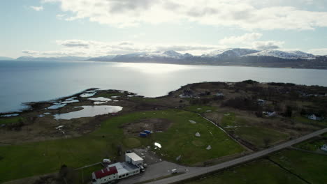 Aerial-view-of-a-Golf-course-with-a-scenic-Norwegian-Landscape-and-snow-covered-mountains