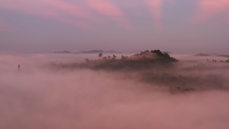 Aerial-view-above-the-mist-to-see-a-magic-sunrise-with-blue-and-pink-colors-and-ray-of-sunshine-behind-mountains