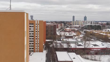 Drone-Footage-Flying-Through-Red-And-Orange-High-Rise-Apartment-Commercial-Buildings-In-Akalla-Stockholm,-Sweden-Showing-Snow-Covered-Town-District-Winterscape-And-Cloudy-Sky
