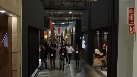 salone-del-mobile-walking-corridor-among-designers-booths,-aerial-like-shot,-camera-high-up,-people-walking-around-and-talking,-4K-50-fps-easy-to-slow-motion