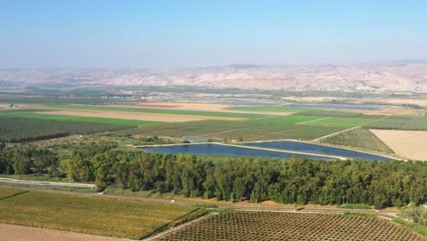 Large-blue-lakes-among-the-green-farmlands-and-the-dense-forests-with-the-high-mountains-of-northern-Israel-in-the-background-on-a-sunny-day-as-several-cars-drive-on-a-road