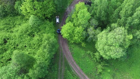 Local-tractor-preparing-to-drag-out-broken-vehicle-from-forest-race-track,-aerial-view