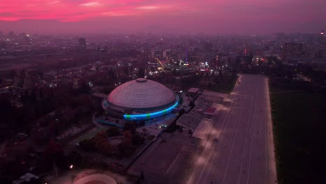 Focus-on-Movistar-arena-stadium-under-pink-sunset-sky-in-middle-of-urban-downtown-of-Santiago,-Chile