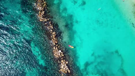Overhead-jib-up-view-of-a-couple-in-a-Kayak-in-the-waters-of-Mambo-Beach-with-a-breakwater-on-the-side,-Curacao,-Dutch-Caribbean-island
