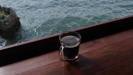 Cup-Of-Brewed-Black-Coffee-On-Wooden-Platform-By-The-Sea