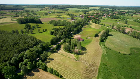 Flying-over-a-Beautiful-Rural-Countryside-Town-in-the-Region-of-Warmian-Masurian-Poland,-Road-Through-Vast-Green-Lands,-Wood-Landscape-and-Local-Homes
