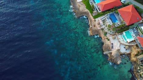 Overhead-dolly-in-aerial-view-of-mansions-on-the-shore-of-Jan-Thiel-Beach,-Curacao,-Dutch-Caribbean-island-of-the-Caribbean