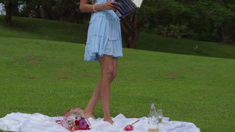 A-young-woman-walking-wwhile-opening-her-book-in-a-park-picnic-setting