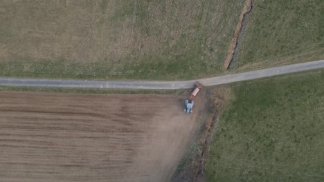 Top-down-aerial-footage-of-a-farmer-starting-to-prepare-a-dry-field-in-a-blue-tractor