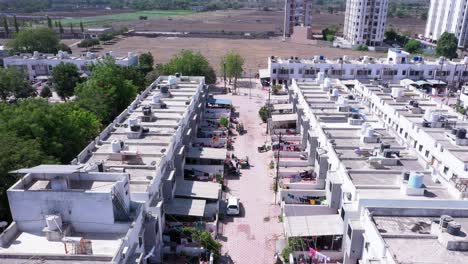 Aerial-footage-flying-over-houses-and-streets-in-House-Complex-City-of-Rajkot-in-India-community-surrounded-by-green-fields-and-rooftops,-blue-clear-sky-sunny-day