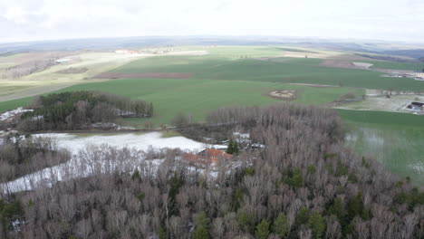Secluded-farm-ranch-in-leafless-tree-grove-and-snowy-field,-Czechia
