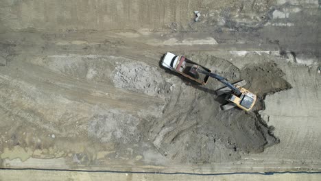Aerial-view-of-a-tractor-filling-a-dumper-truck-with-soil-at-construction-site,-project-in-progress