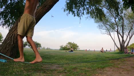 Lateral-shot-of-adult-male-legs-balancing-on-slack-line-at-park-outdoors