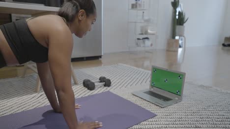 A-static-shot-of-a-black-female-doing-stretches-in-front-of-a-green-screen-on-the-floor-of-her-house-in-the-kitchen