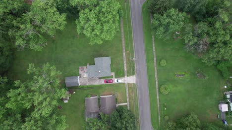 Aerial-drone-landing-shot-over-a-residential-houses-surrounded-by-lush-green-vegetation-by-the-side-of-a-road-at-daytime