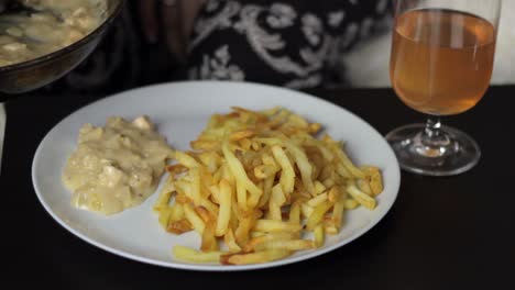 A-person-serving-creamy-sauce-with-a-basting-spoon-on-a-plate-with-French-fries,-close-up-static