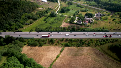 Aerial-Tracking-View-of-Fluid-Cars-and-trucks-Traffic-on-Multi-Lanes-Countryside-Highway,-Surrounded-by-Fields-Green-Lands-Trees-and-Suburban-Homes,-Travel-and-Transport-in-Gdynia-Poland