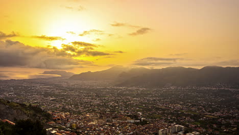 High-angle-shot-of-Palermo-city-in-Sicily,-Italy-in-the-foreground-and-mountain-range-in-the-background-with-sun-setting-over-the-horizon