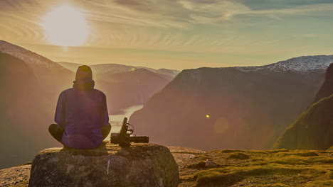 Zeitrafferaufnahme-Mit-Einem-Mann,-Der-Auf-Einem-Felsen-Sitzt-Und-Die-Bergkette-In-Norwegen-Bei-Sonnenuntergang-Beobachtet