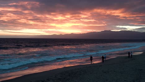 Santa-Barbara-California-coastline-during-sunset-as-people-stroll-the-beach,-Wide-handheld-shot