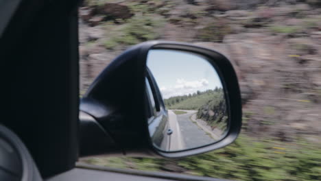 Rear-view-through-side-mirror-on-mountain-road