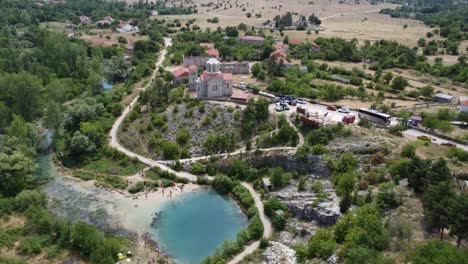 drone-pans-from-above-down-to-the-famous-cetina-spring-in-croatia,-a-small-church-towers-over-the-lake
