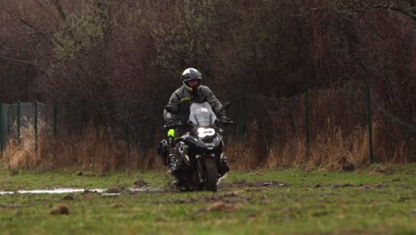 Motorbike-Splashing-Water-Ponds-and-Mud,-Rainy-Slow-Motion-Driver-in-Black-Raincoat-and-Helmet,-Extreme-Cross-in-Fields