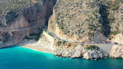 aerial-drone-panning-out-revealing-a-coastal-road-at-Kaputas-Beach-in-Kas-Turkey-on-a-sunny-afternoon-day-during-summer-as-tourists-relax-along-the-Mediterranean-Sea-in-the-summer-surrounded-by-cliffs