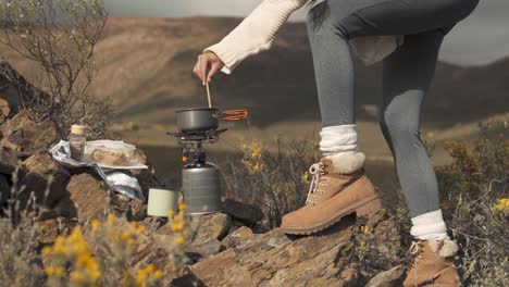 Side-view-slow-motion-footage-of-a-woman-cooking-noodles-in-a-tiny-pot-on-top-of-a-mountain