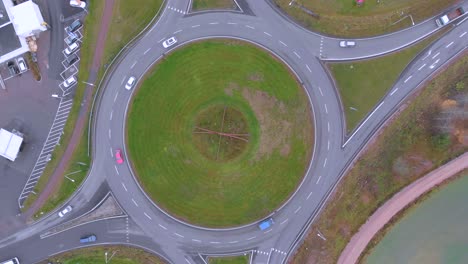 Top-view-of-a-drone-footage-with-cars-driving-in-and-out-of-a-roundabout,-on-a-cloudy-day-in-October