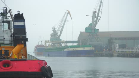 Port-cranes-loading-dry-cargo-ship-at-Port-of-Liepaja-in-foggy-day,-medium-shot