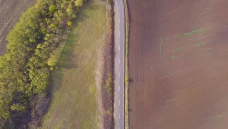 Flying-over-a-road-in-a-rural-with-a-forest-looking-down-from-a-drone