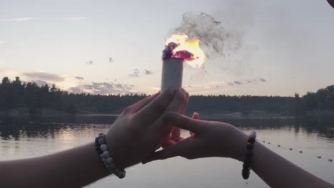 Two-person-hold-a-colored-smoke-bomb-in-hands-while-walking-into-a-lake,-slow-motion