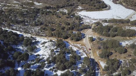 Aerial-shot-of-a-car-driving-through-a-road-surrounded-by-snowed-pines-in-Spain