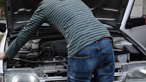Young-man-works-on-repairing-an-old-broken-down-car-engine