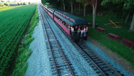 Steam-Train-at-Picnic-Area,-Pulling-out-of-Picnic-Area,-in-Amish-Countryside-as-seen-by-Drone