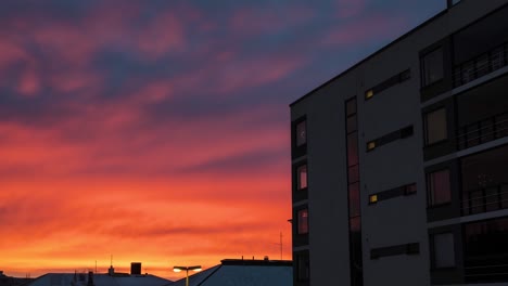 4K-Zeitraffer-Eines-Farbenfrohen-Sonnenuntergangs-Mit-Kräftigen-Roten-Farben-Am-Himmel-Und-Spiegelungen-An-Den-Fenstern-Eines-Neuen-Wohnhauses
